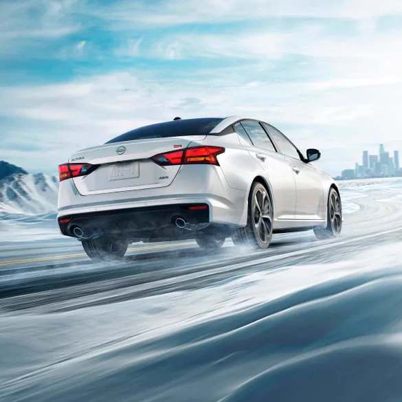 2027 Nissan Altima in white seen from behind driving in snowy landscape illustrating all-wheel drive at Nissan of Dearborn in Dearborn MI